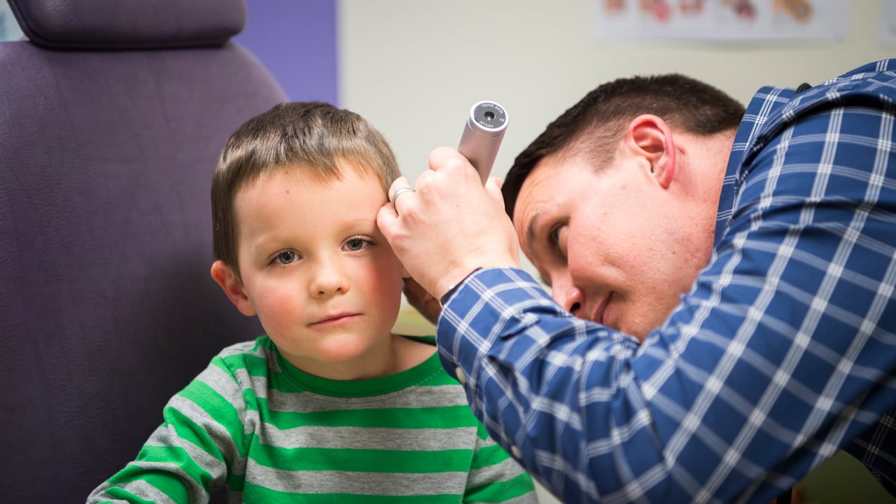 A young child gets his ears checked by a doctor during an office visit. 