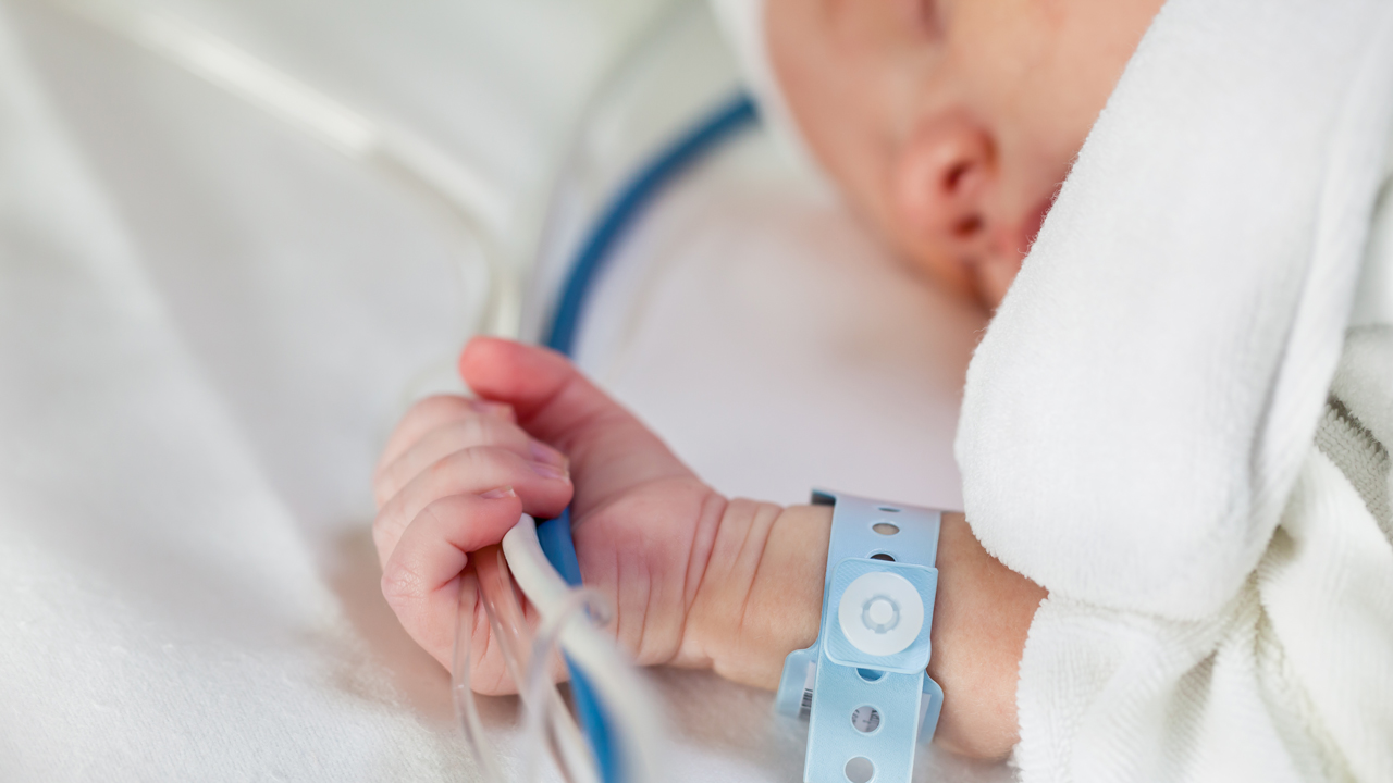 Close-up of a newborn baby holding life-support hoses and cables tight in his hand