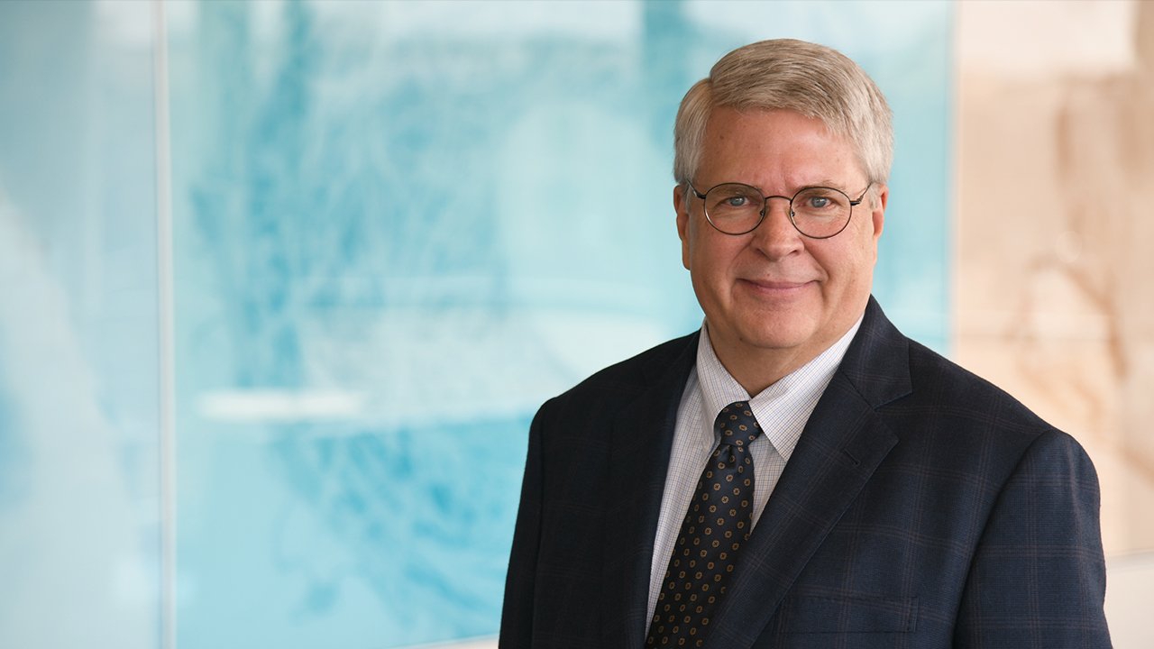 Photo of Stephen Daniels smiling against blue glass background