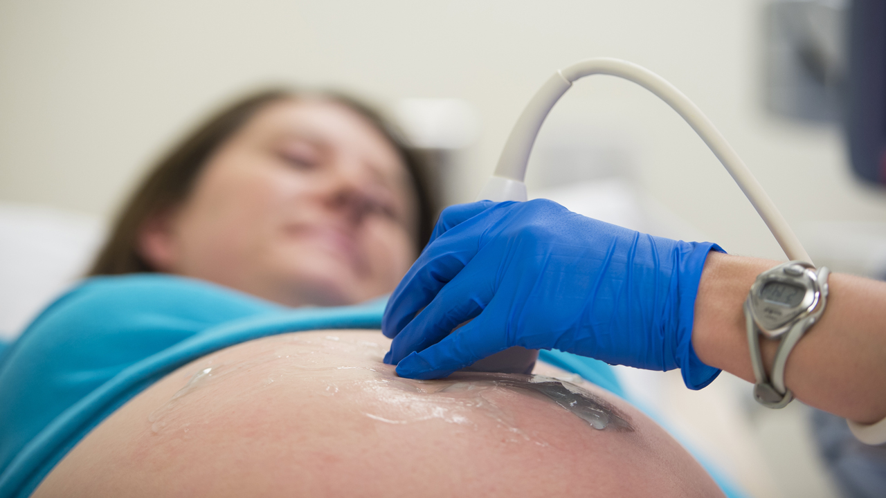 A pregnant woman laying in a hospital bed receives an ultrasound.