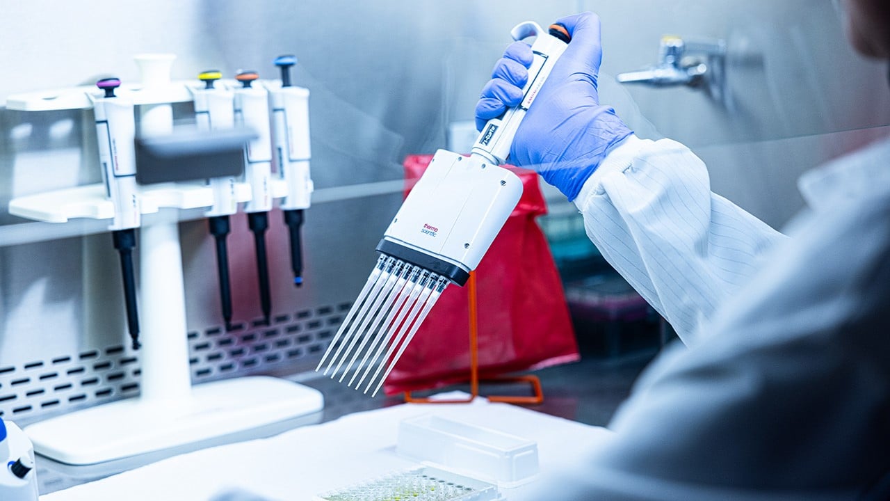 A scientist at Children’s Hospital Colorado using a multi-channel pipette to dispense samples into a tray in a laboratory setting.