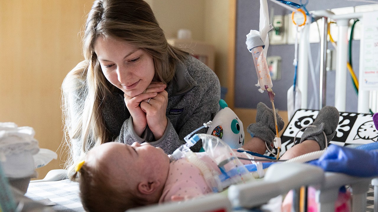 A parent in the Children’s Hospital Colorado NICU looks at their baby, who lies in their bed.