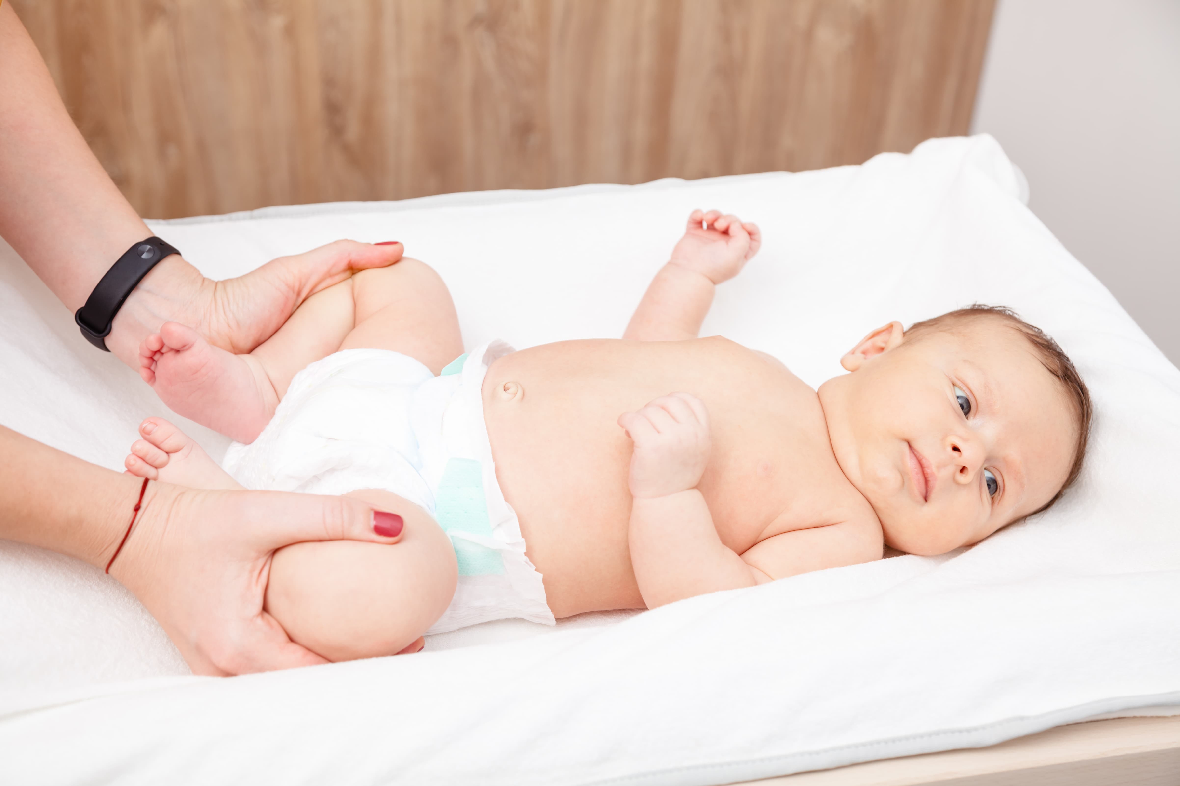 An infant lying on a changing table while an adult's hands gently hold the baby's legs.