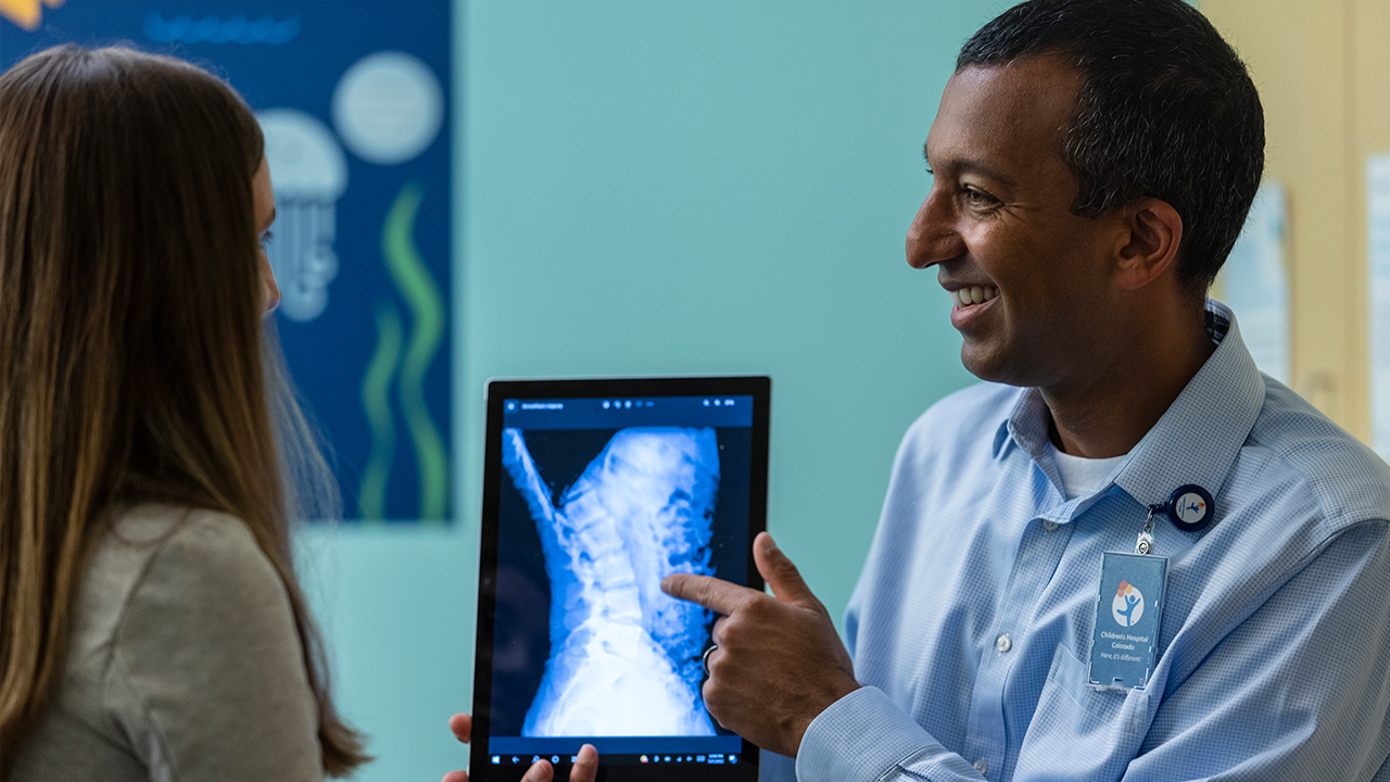 Dr. Sumeet Garg points to an X-ray image of a spine while talking with a patient.