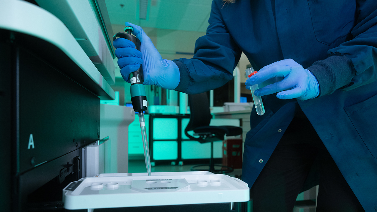 A person in a lab coat using a pipette to transfer a liquid into a test tray in a laboratory setting at Children’s Hospital Colorado.