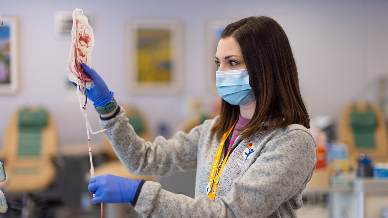 A healthcare worker in a mask examines a blood bag at Children’s Hospital Colorado.