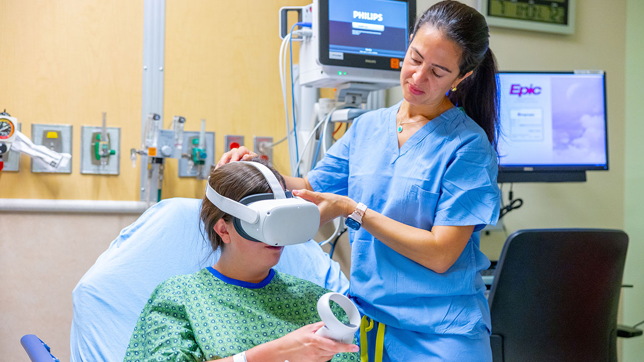 A provider puts a virtual reality headset over the eyes or a teenage patient in a hospital bed.