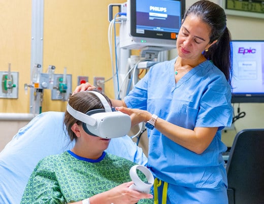 A provider puts a virtual reality headset over the eyes or a teenage patient in a hospital bed.