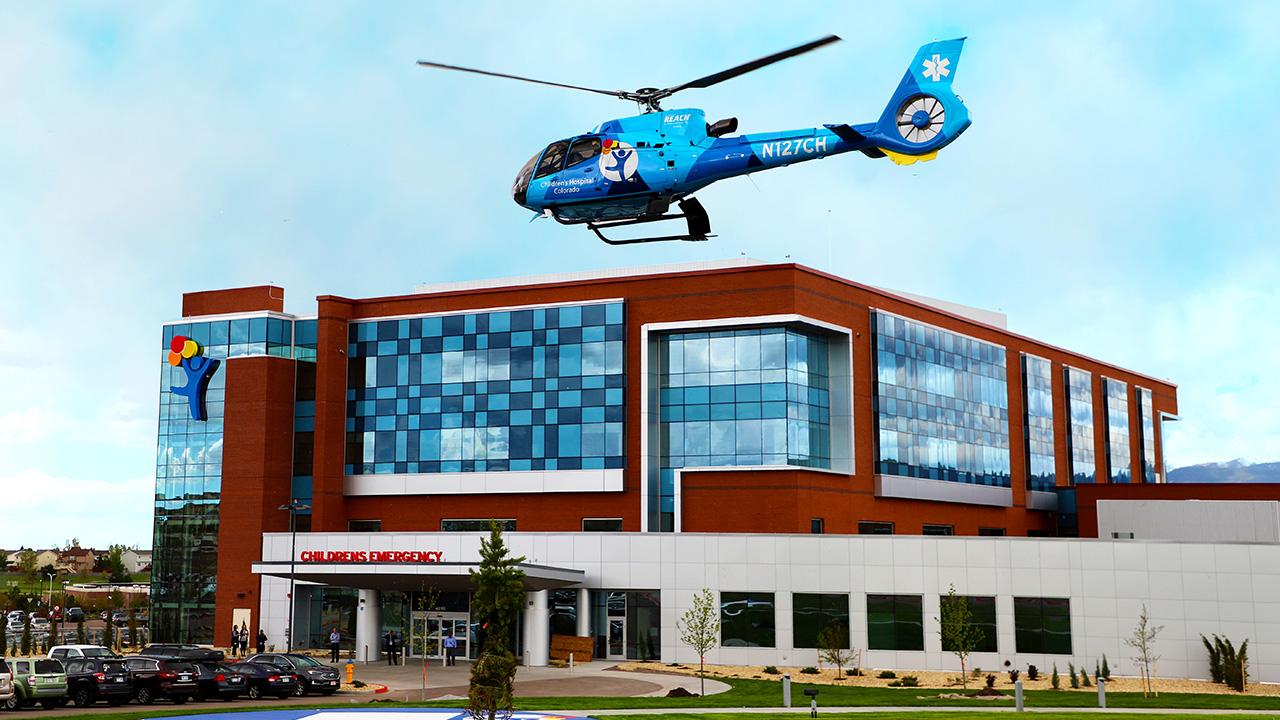 A Children’s Hospital Colorado helicopter flies above a Children’s Colorado hospital building.