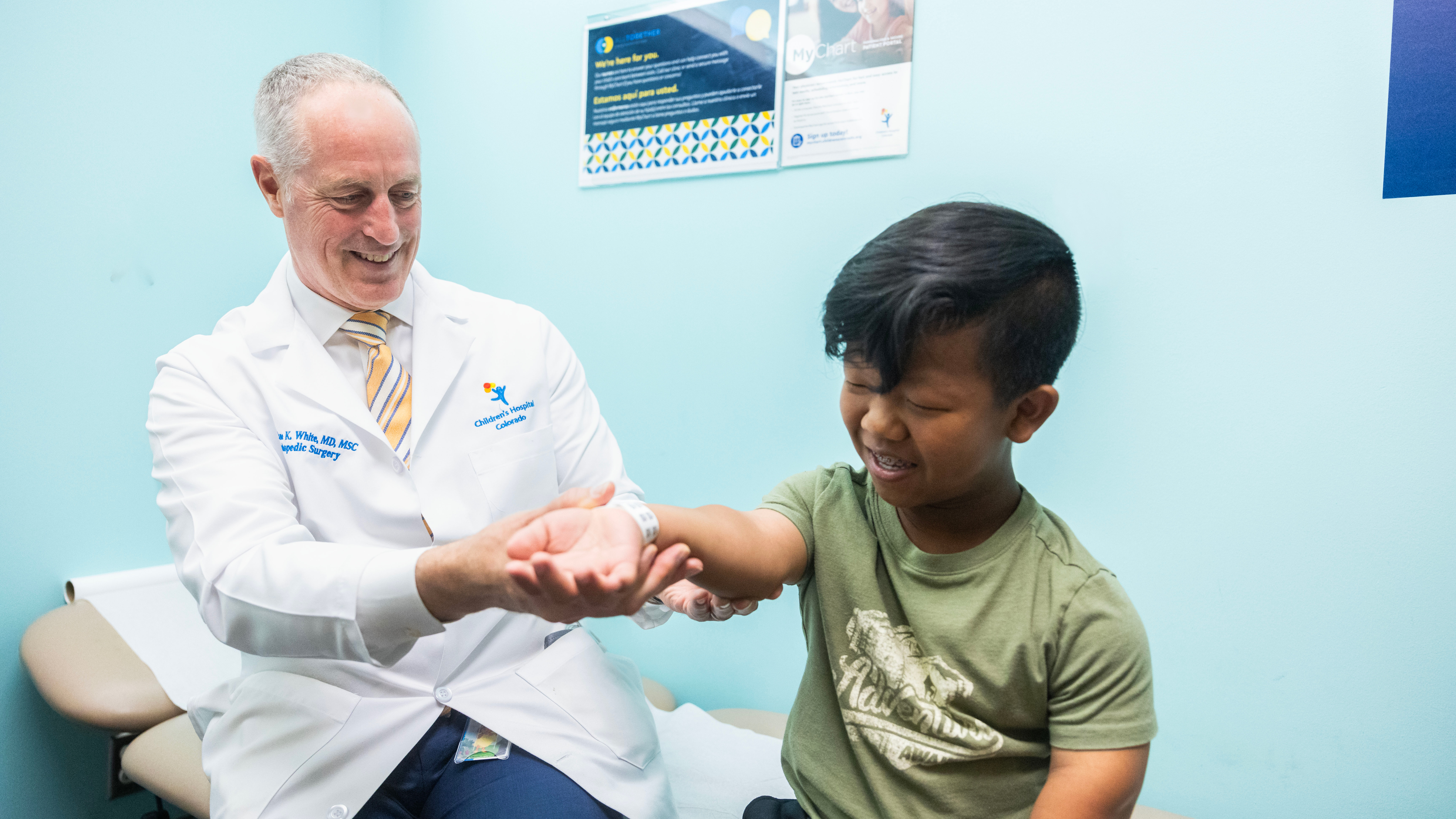 An orthopedic surgeon smiles while he examines a child's arm and the child smiles.