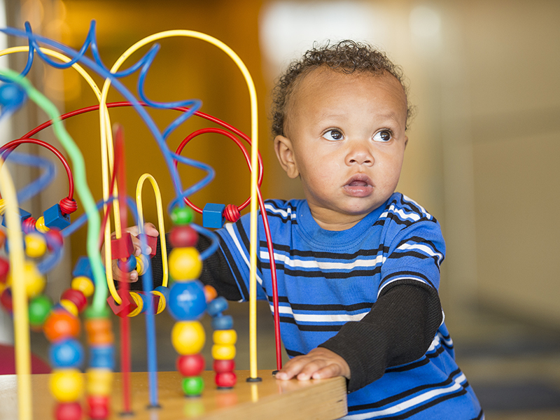 A toddler boy in a blue and black striped shirt plays with a wooden bead maze toy.