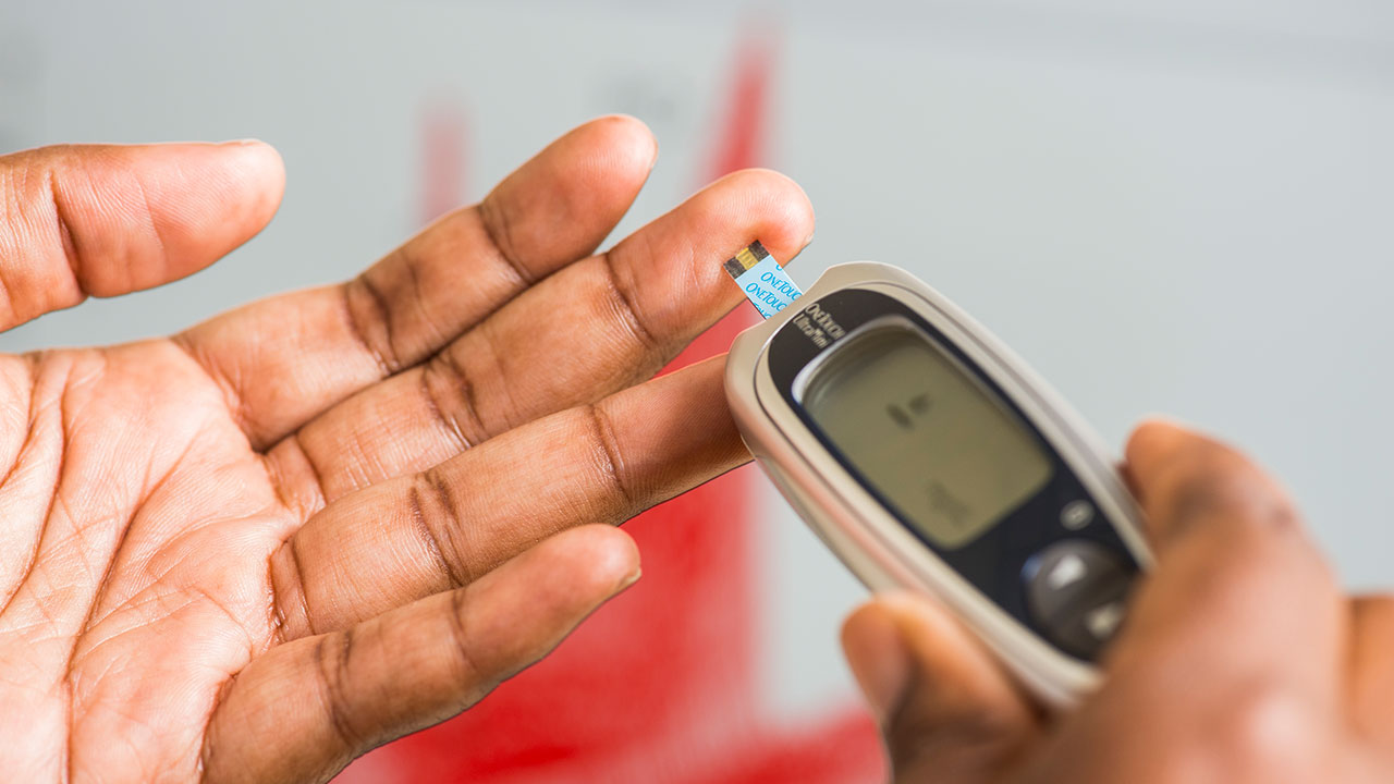 A left hand being checked by a finger stick check device to check blood sugar levels.