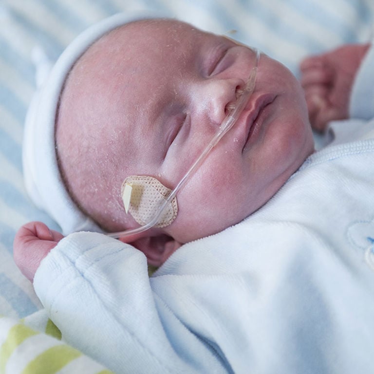 Close-up of sleeping baby with oxygen tube in nostrils. Dressed in blue, lying in the NICU.