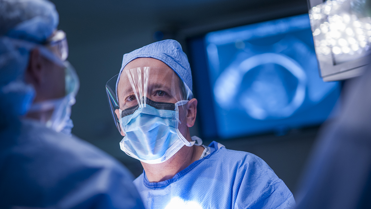 A surgeon operates wearing a clear face shield