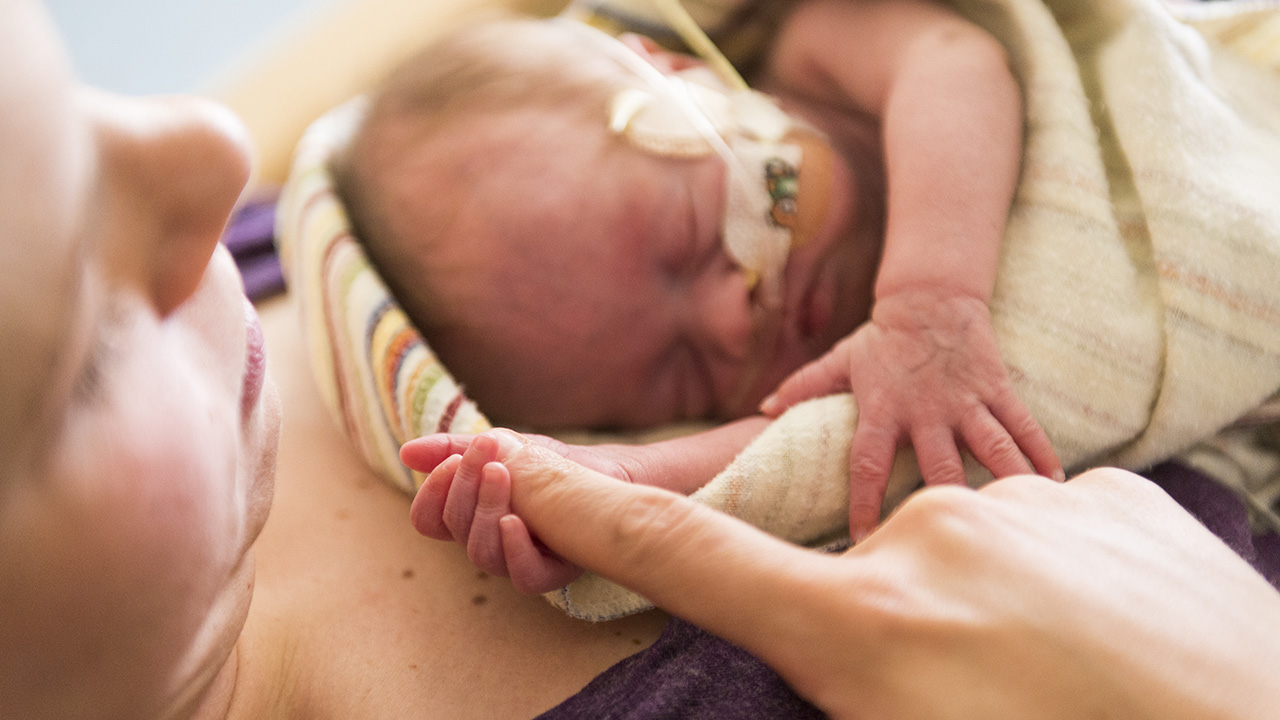 Newborn with oxygen holds finger of mother while laying on her chest