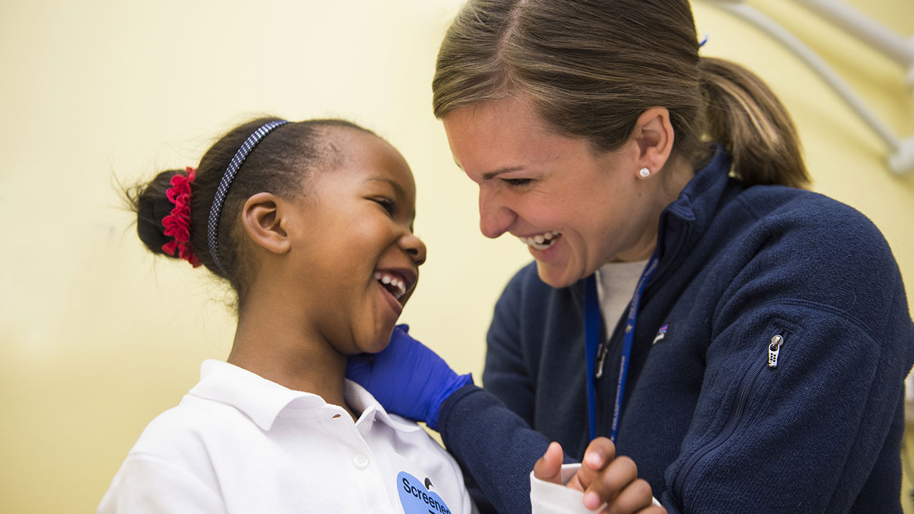 A healthcare provider and their pediatric patient smile at each other.