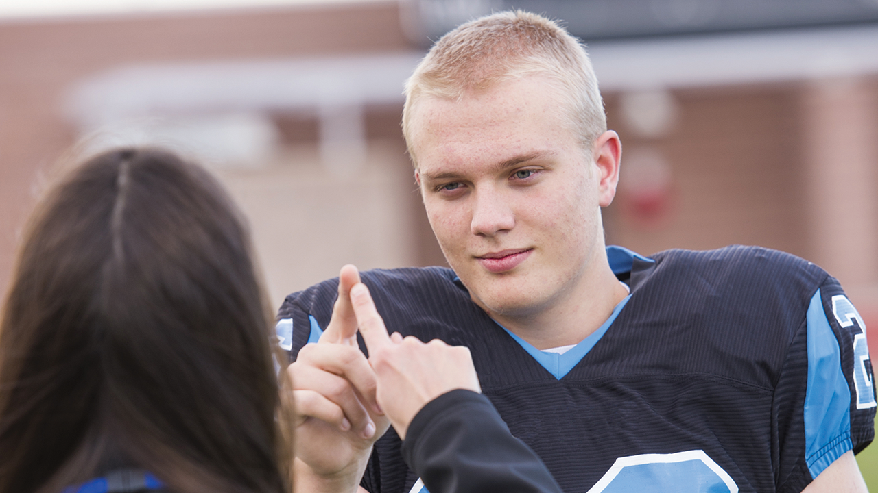 Teenaged football player touching index fingers with athletic trainer