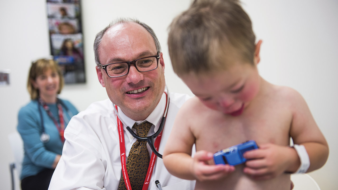 Dr. Dunbar Ivy Listens to a toddler's heart while the child plays with a toy car.