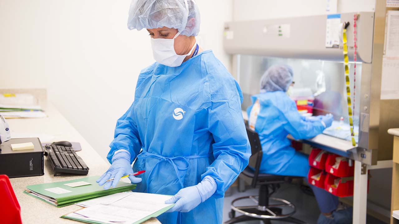 Researchers working with papers in blue scrubs and protective headgear.