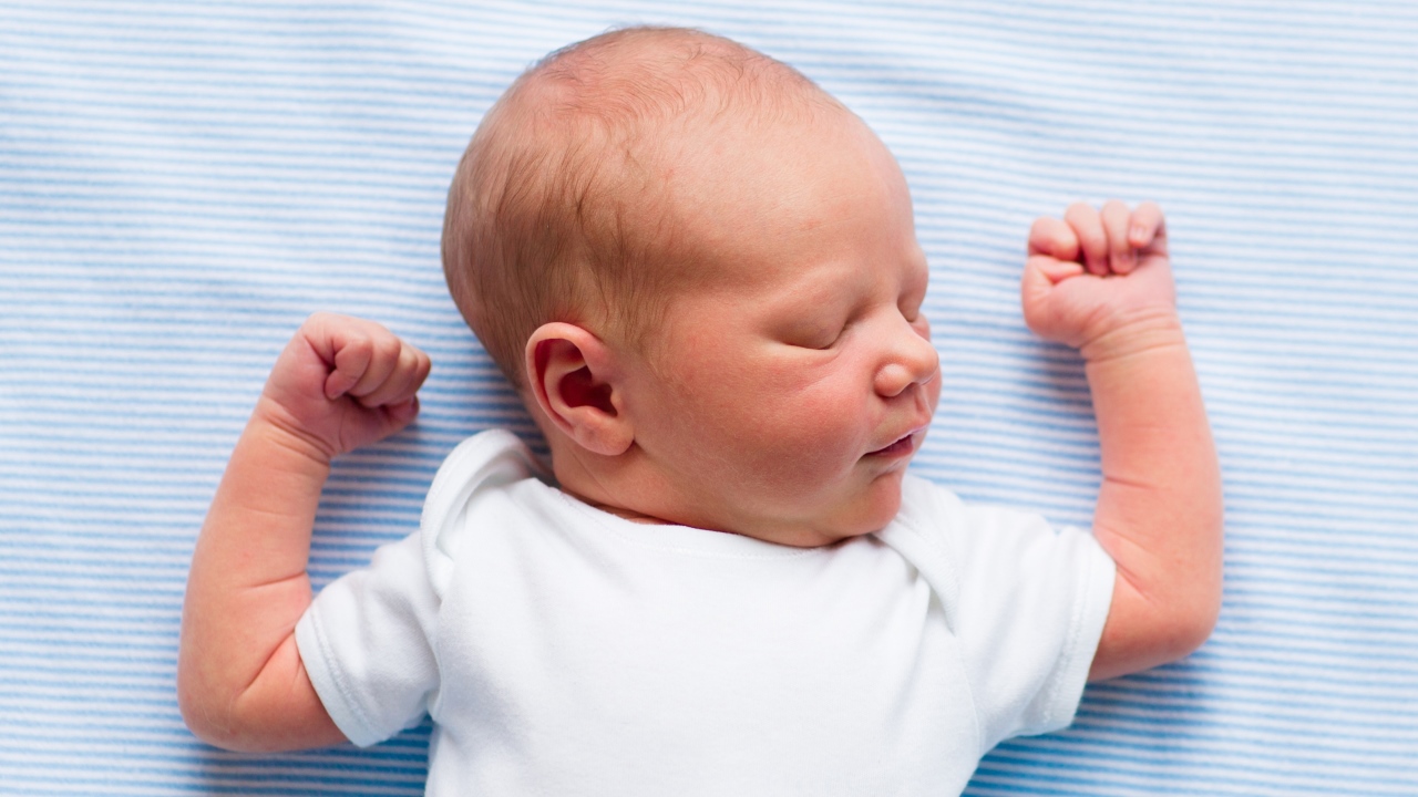 A baby sleeps on its back in a crib with hands up near head.