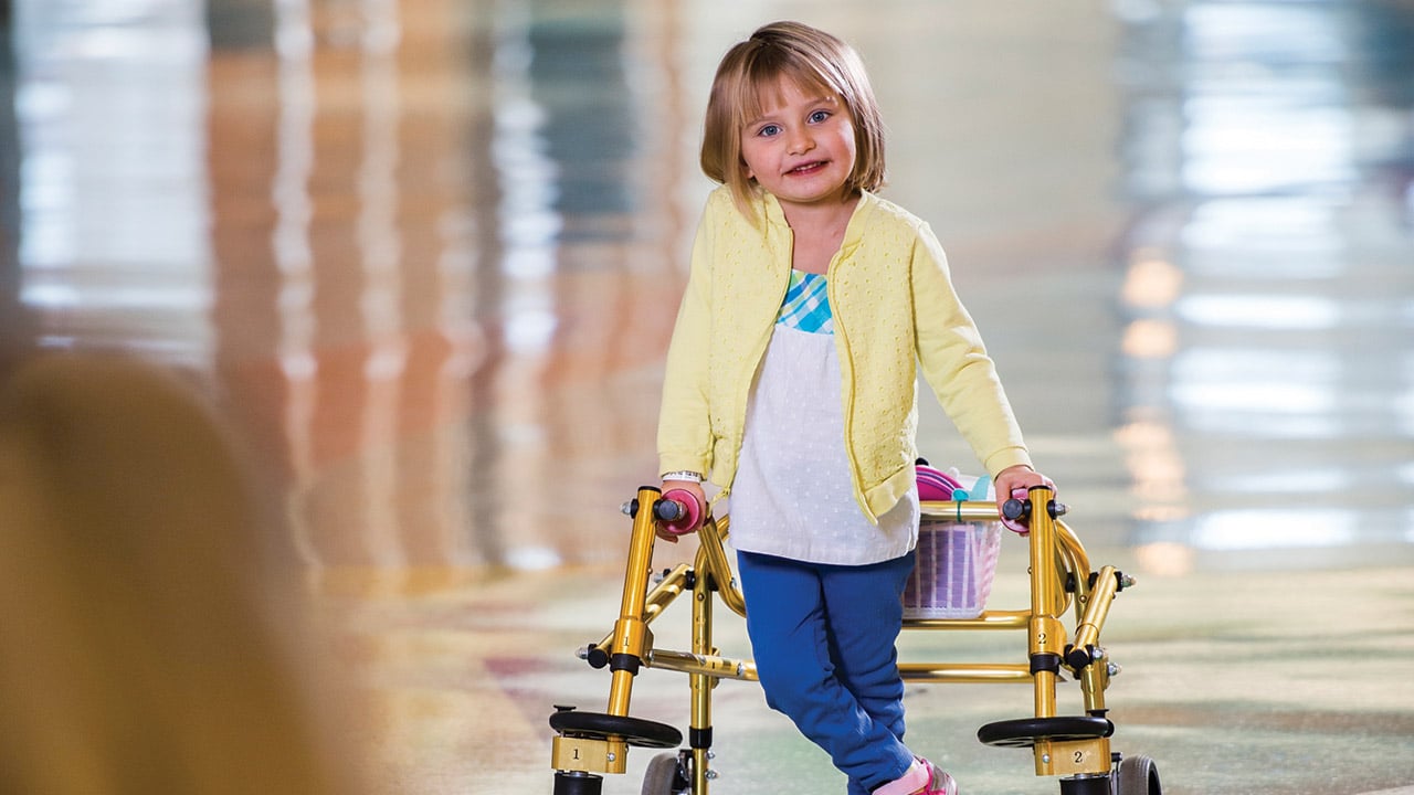 Lexi, a patient at Children's Hospital Colorado, stands holding a walker.